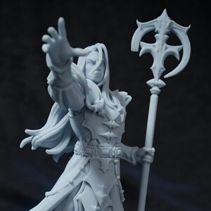 May include: A white painted miniature figurine of a person wearing a long robe and holding a staff with a curved top. The figurine is standing on a round base.