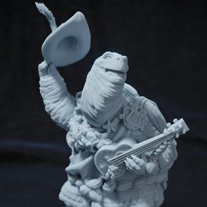 以下が含まれることがあります： ウクレレを弾き、帽子を持っているカメの薄い青色の置物。カメはレイと装飾的な衣装を着ています。置物は濃い灰色の台座にあります。