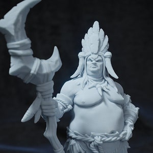 May include: A white painted miniature figurine of a large, stout, humanoid figure wearing a feathered headdress and holding a staff with a crescent moon-shaped top. The figure is standing on a round base.