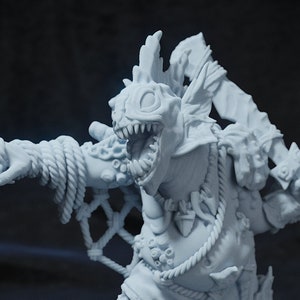 May include: A white painted miniature figurine of a monstrous creature with a fish-like head, holding a sword and a net. The creature is wearing a tattered cloth and has a rope belt. The figurine is standing on a round base.