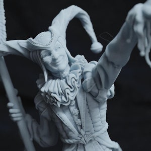 May include: A detailed, light-coloured figurine of a jester, holding a banner and gesturing with one arm raised. The jester wears a ruffled collar, a pointed hat, and a smiling expression. The banner has an ornate design.