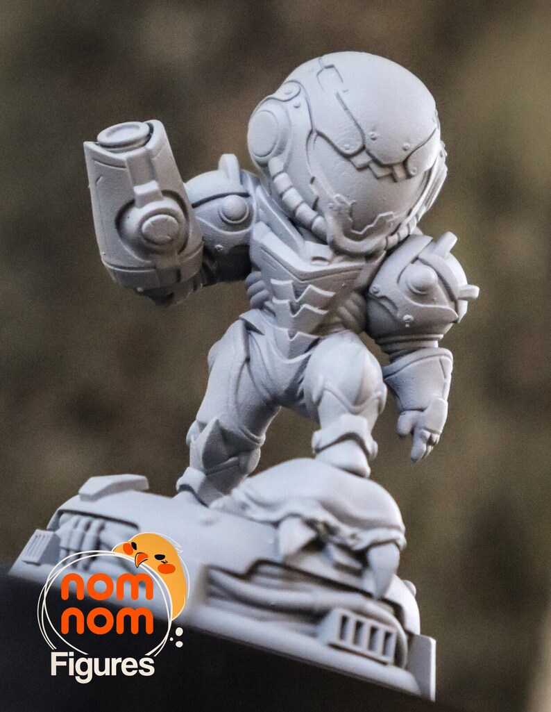 May include: A gray, 3D printed figurine of a space-suited character, standing on a base with the words "nom nom figures" printed on it.