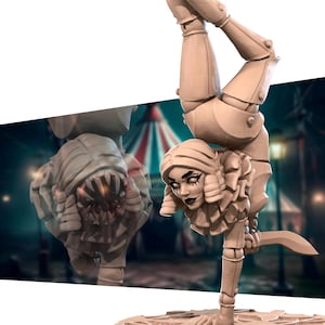 May include: A beige figurine of a performer in a handstand, holding a knife. The figure has a stylized face with dark makeup and a ruffled collar. A monster-like figure is partially visible in the background, with a circus tent in the distance.
