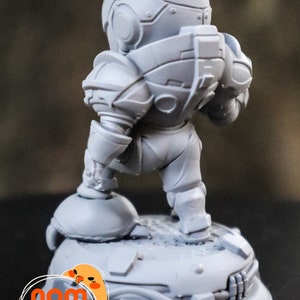 May include: A gray, detailed, 3D printed miniature figure of a robot wearing a helmet and standing on a round base. The base has a textured surface and the text "CPT" is printed on it.