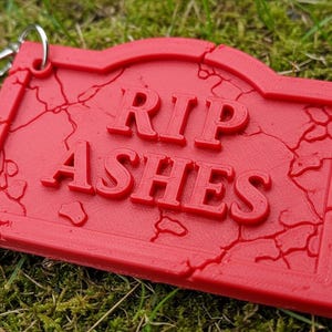 May include: Red plastic keychain with a cracked tombstone design that reads "RIP Ashes".