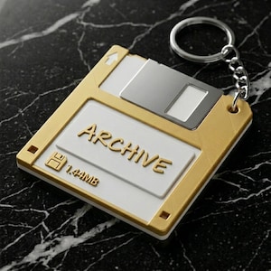 May include: A gold and white floppy disk keychain with the word "ARCHIVE" in gold lettering. The keychain has a silver key ring and chain. The floppy disk reads "1.44MB".