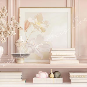 Op de afbeelding: Een roze schoorsteenmantel met een witte vaas gevuld met gedroogde bloemen, een ingelijst bloemenprint, een stapel boeken, een decoratieve kandelaar en twee kleine decoratieve voorwerpen.