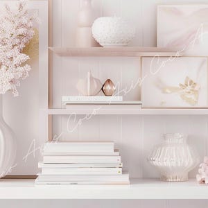 Op de afbeelding: Een wit rek met drie planken, versierd met een witte vaas met roze bloemen, een stapel witte boeken, een wit en gouden decoratief object, een heldere glazen vaas en een roze bloemenarrangement.