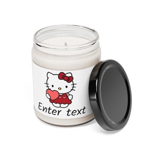Puede incluir: Un tarro de vela blanco con una tapa negra. El tarro tiene una etiqueta blanca con una imagen de dibujos animados de Hello Kitty sosteniendo un corazón rojo. La etiqueta también tiene el texto "Enter text".