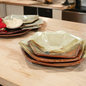 May include: A set of four ceramic plates in a rustic style. The plates are stacked on top of each other and have a brown, orange, and green glaze. The plates are shaped like a hexagon.