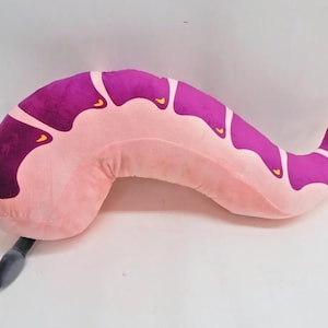 May include: A pink and purple plush pillow shaped like a worm. The pillow has a long, curved body with a pointed tail. The pillow is soft and cuddly and would be perfect for a child's bedroom.