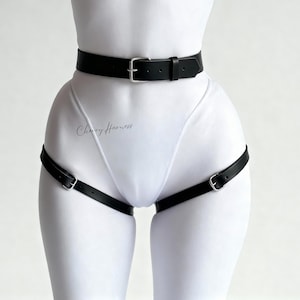 May include: Black leather body harness with silver-tone buckles. The harness includes a waist belt and leg straps. The text "Cherry Harness" is visible on the garment. The harness is designed to be worn over clothing.