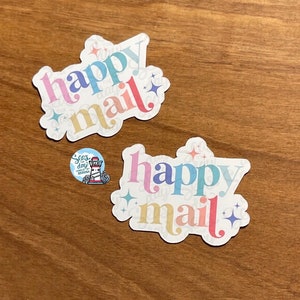 May include: Two white stickers with the text "happy mail" in rainbow colors and sparkly accents.