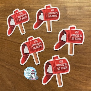 May include: Five red and white mailbox stickers with the text "Your completed TPG has arrived!" on each. The stickers are on a wooden surface.