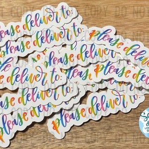 May include: A pile of rainbow-colored stickers with the text "Please deliver to" on each sticker. The stickers are on a wooden surface.