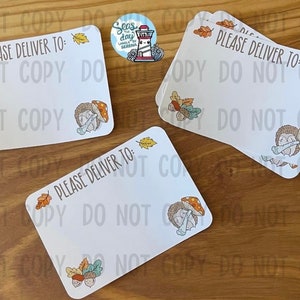 May include: Three white cards with the text "Please Deliver To:" and a hedgehog illustration with mushrooms and leaves. The cards are on a brown wooden surface.