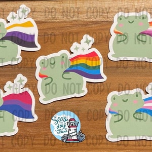 May include: Five frog stickers with different pride flags. Each frog is green with a white outline and a small smile. The flags are rainbow, bisexual, transgender, non-binary, and lesbian.