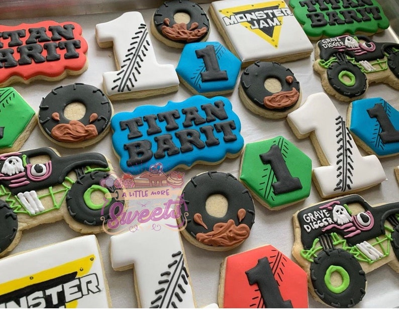 May include: A collection of decorated sugar cookies featuring monster trucks, the words "Titan Barit", "Monster Jam", and "Grave Digger", and the number "1". The cookies are decorated with various colors, including red, blue, green, black, and white.