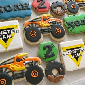 May include: A collection of decorated sugar cookies featuring monster trucks, the name "Noah", and the words "Monster Jam". The cookies are decorated with bright colors, including orange, yellow, green, blue, and black.