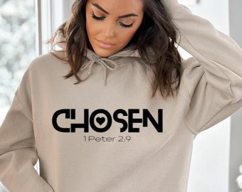 May include: A beige hoodie with a front pocket and drawstring. The word "CHOSEN" is printed in black across the chest, with a heart symbol replacing the "O". Below the word is the text "1 Peter 2:9".