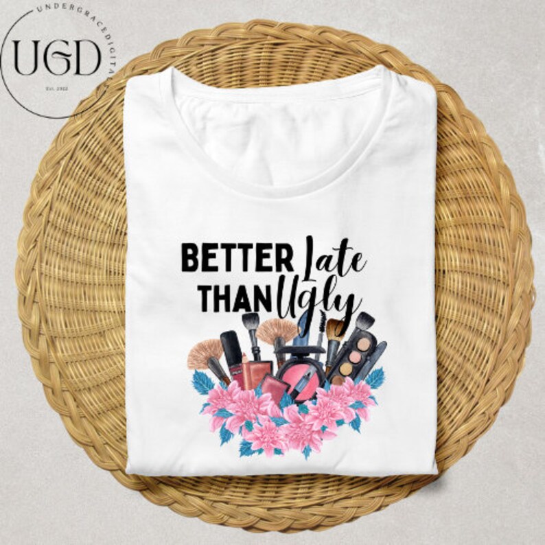 Puede incluir: Camiseta blanca con la frase negra "BETTER Late THAN Ugly". El dise&ntilde;o incluye brochas de maquillaje, cosm&eacute;ticos y flores rosas. La camiseta est&aacute; doblada sobre una superficie redonda y tejida.