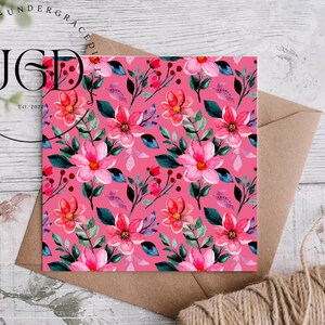 Op de afbeelding: Een vierkante kaart met een levendig roze bloemenpatroon met roze bloemen in aquarel, groene bladeren en rode bessen. De kaart ligt op een bruine envelop met een touwtje. De tekst "UNDERGRACED" en "Est. 2022" is zichtbaar.