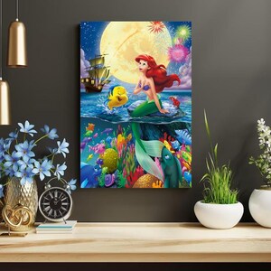 Peut inclure: Une illustration color&eacute;e d'Ariel, la Petite Sir&egrave;ne, nageant dans l'oc&eacute;an avec Polochon. La sc&egrave;ne comprend un navire, une pleine lune et des feux d'artifice.