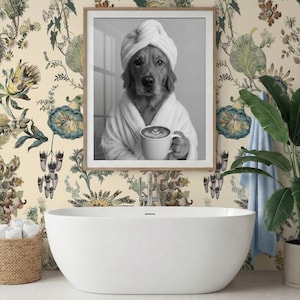 May include: A framed black and white wall art print featuring a dog wearing a white towel wrapped around its head and a white bathrobe, holding a white ceramic mug with latte art. The print is displayed above a white freestanding bathtub.