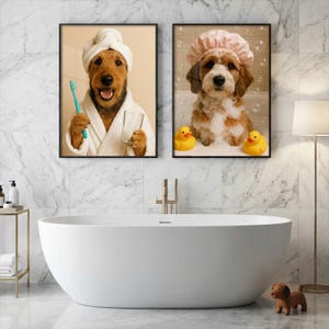 May include: Two framed wall art prints displayed above a white bathtub. The left print shows a brown dog in a white bathrobe and towel wrap holding a blue toothbrush and glass. The right print shows a brown and white dog in a pink shower cap.