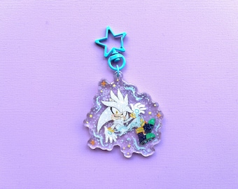 May include: A clear acrylic charm depicting a cartoon character with white fur and spiky hair, wearing blue and green boots. The charm is attached to a teal star-shaped clasp. The background is a solid lilac colour.