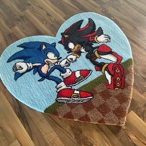Pode incluir: Um tapete em forma de coração com Sonic the Hedgehog e Shadow the Hedgehog. O tapete é feito de um material macio e felpudo e tem um fundo azul com um padrão xadrez marrom e vermelho.