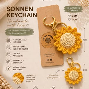 Könnte beinhalten: Zwei gehäkelte Sonnenblumen-Schlüsselanhänger mit gelben Blütenblättern und cremefarbenen Mitten, befestigt an goldenen Karabinerhaken. Die Anhänger sind auf einer Pappkarte mit Text wie SONNEN KEYCHAIN und den Größen 5 cm und 7 cm abgebildet.