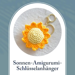 Könnte beinhalten: Ein gehäkelter Sonnenblumen-Schlüsselanhänger mit gelber Mitte und gelben Blütenblättern. Der Schlüsselanhänger ist an einem goldenen Schlüsselring befestigt.