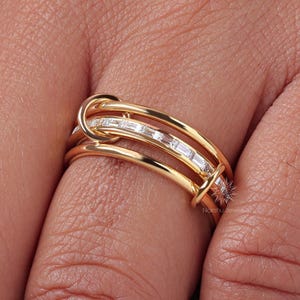 May include: A gold ring with a unique design. The ring features a series of parallel bands, with a central section adorned with rectangular-cut gemstones. The ring is shown on a person's finger.