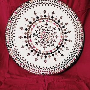 May include: A round, white mosaic mirror with a geometric design in shades of brown, pink, and black. The mirror is surrounded by a decorative border of brown and white.