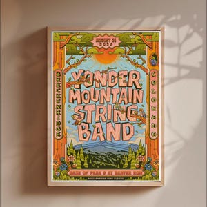 May include: A framed concert poster for Yonder Mountain String Band in Breckenridge, Colorado, on 21 August 2036. The artwork features a sun, mountains, pine trees, and birds in a colour palette of orange, green, and blue with bold lettering.
