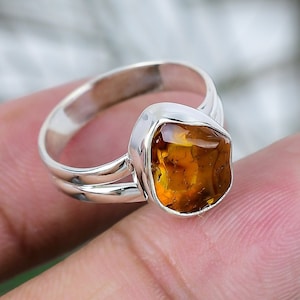 May include: A silver ring with a large, amber-colored gemstone. The ring is set on a finger.