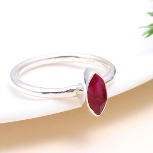 Può includere: Un anello d'argento con una pietra preziosa di rubino a forma di marquise. L'anello è semplice ed elegante.