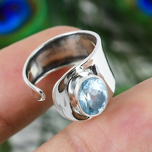 Puede incluir: Un anillo de plata con una piedra preciosa azul claro. El anillo es abierto y ajustable.