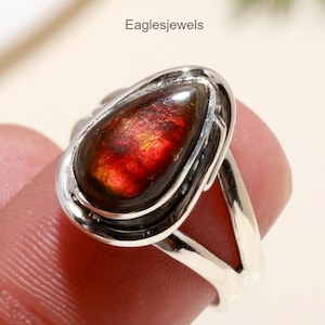 May include: A silver ring with a teardrop-shaped red and brown gemstone set in a silver bezel. The ring has a simple, elegant design.