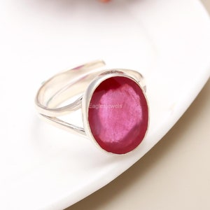 Könnte beinhalten: Ein silberner Ring mit einem großen ovalen Rubin-Edelstein. Der Ring hat ein schlichtes Design mit einem dünnen Band und einem geteilten Band.