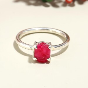 Puede incluir: Un anillo de plata con una piedra preciosa de rubí rojo. El rubí es de corte en bruto y tiene una forma natural irregular.
