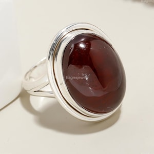 May include: A silver ring featuring a large, oval-shaped, dark red gemstone set in a double-rimmed bezel.