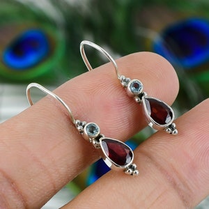 Peut inclure: Une paire de boucles d'oreilles pendantes en argent avec une pierre rouge en forme de larme et une pierre bleue ronde sur chaque boucle d'oreille.