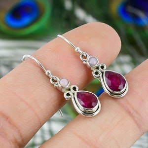 May include: A pair of silver dangle earrings with a pink and red gemstone teardrop design.