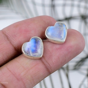 May include: A pair of silver heart-shaped earrings with moonstone inlays. The earrings are small and delicate.