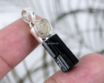 May include: A silver pendant featuring a black tourmaline gemstone and a clear quartz crystal. The pendant is set in a silver setting and has a bail for attaching to a chain.