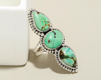 May include: A silver ring with three turquoise stones. The stones are set in a bezel setting and are surrounded by a beaded border. The ring is a statement piece and would be perfect for a boho chic look.