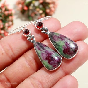 May include: A pair of dangle earrings featuring green and pink ruby zoisite gemstones with red garnet accents. The earrings are made of sterling silver.