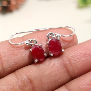 Pode incluir: Um par de brincos de prata com pedras preciosas ovaladas vermelhas. Os brincos têm um design simples com fecho de gancho.